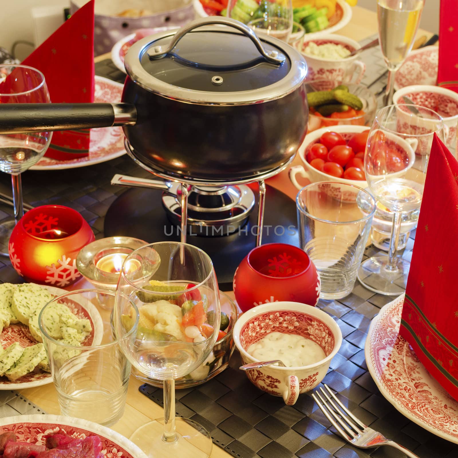 A well-laid table with a fondue caquelon, vegatables and dishes. Square format.
