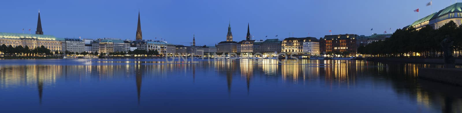 Panorama picture of the Binnenalster in Hamburg at the blue hour. The dark trees on the right side keep the viewers attention focused on the center of the picture.