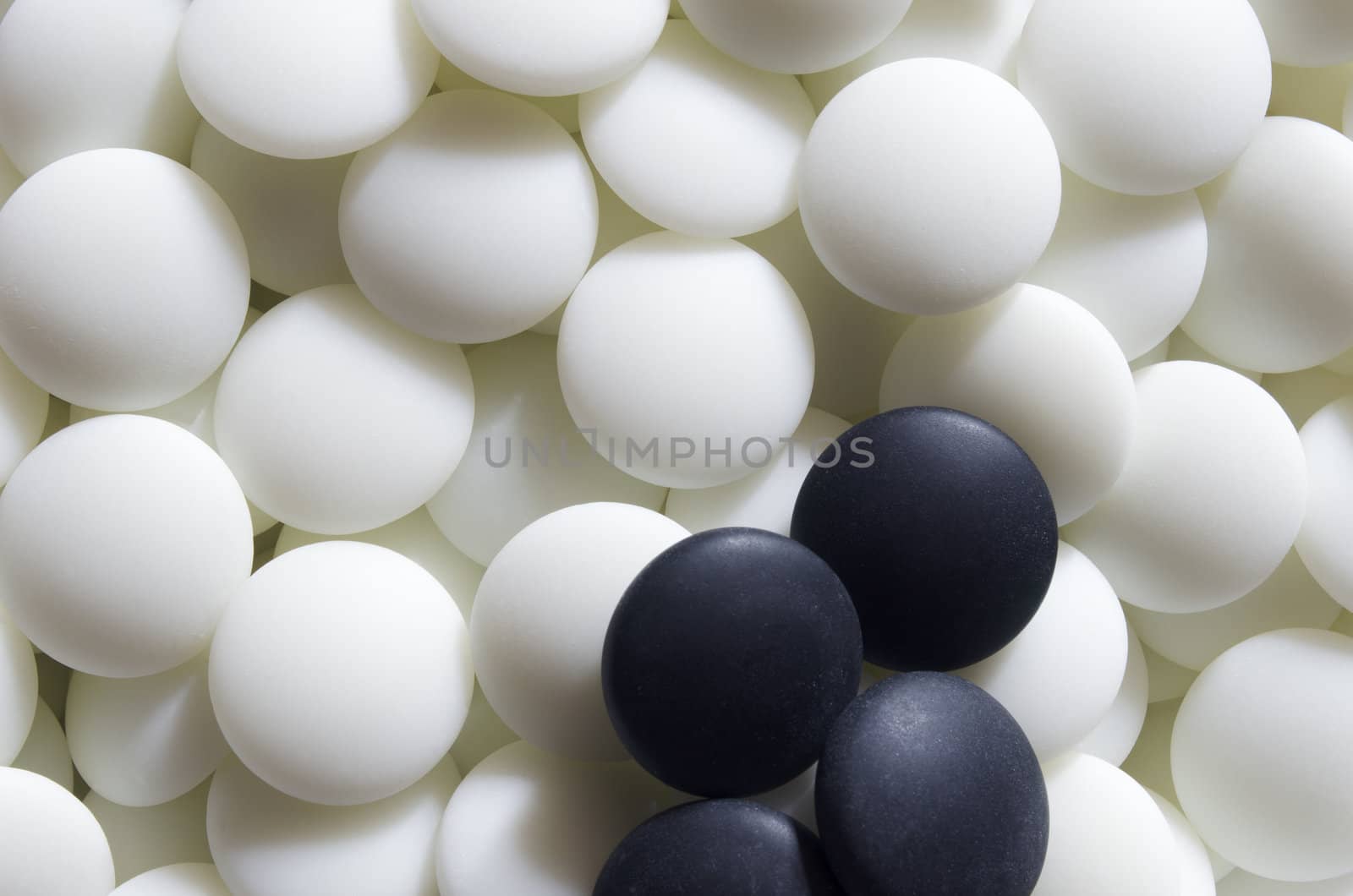 Some black go stones on a pile of white ones. Go is a traditional Asian strategic board game. It is considered to be of the oldest games in the world.