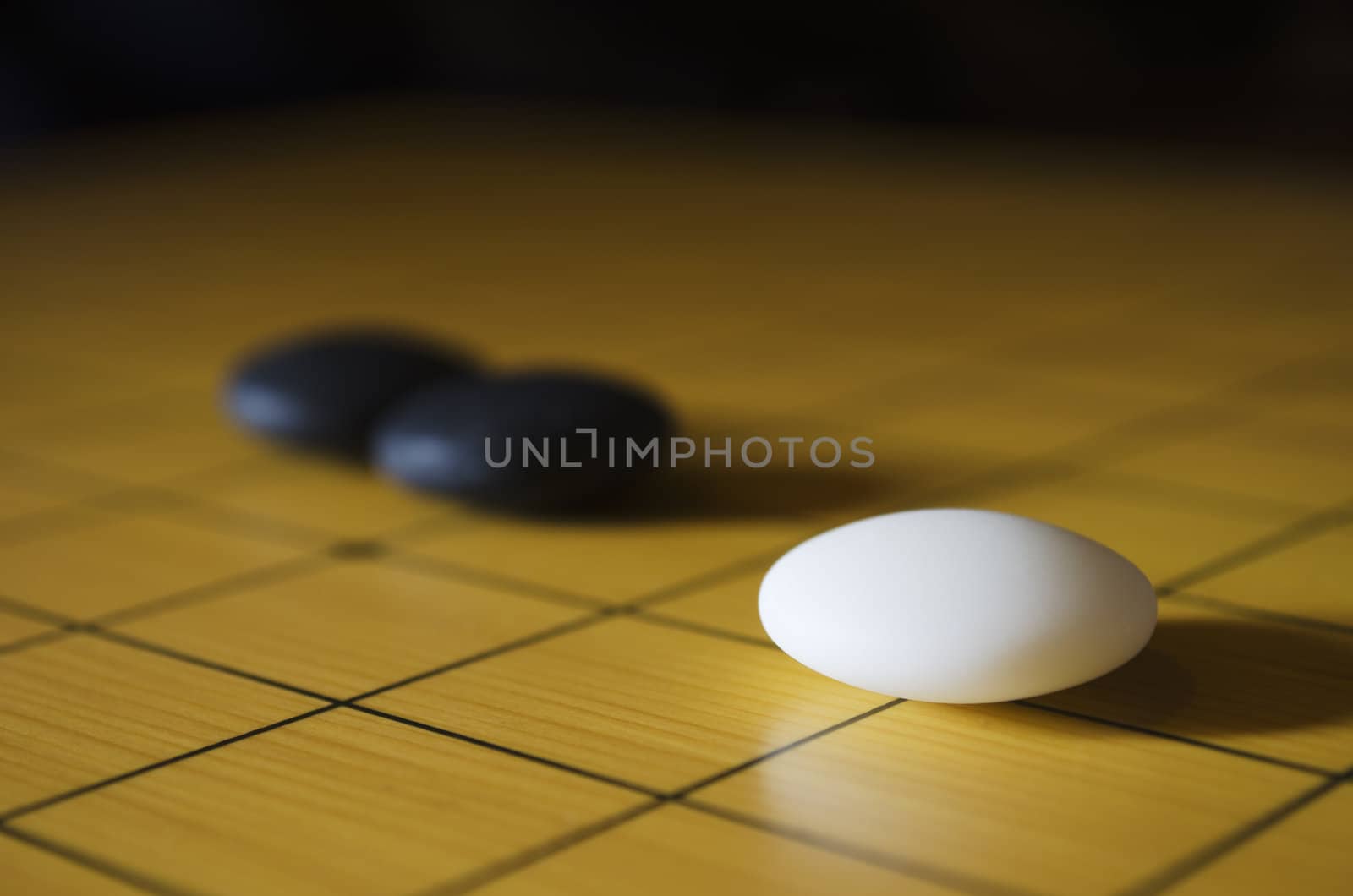Closeup shot of a white and two black go stones on the goban. Go is an ancient traditional Asian board game. Shallow depth of field.