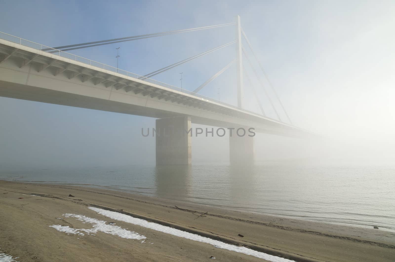 Winter morning by Danube river with bridge in fog