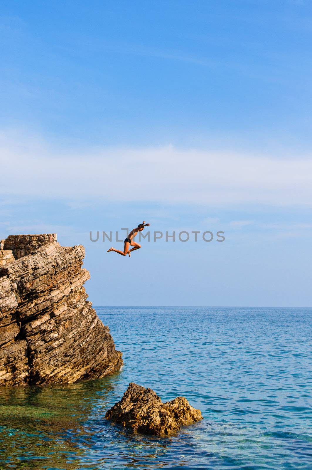 Boy Jumping Off Cliff Into Blue Water at sunset