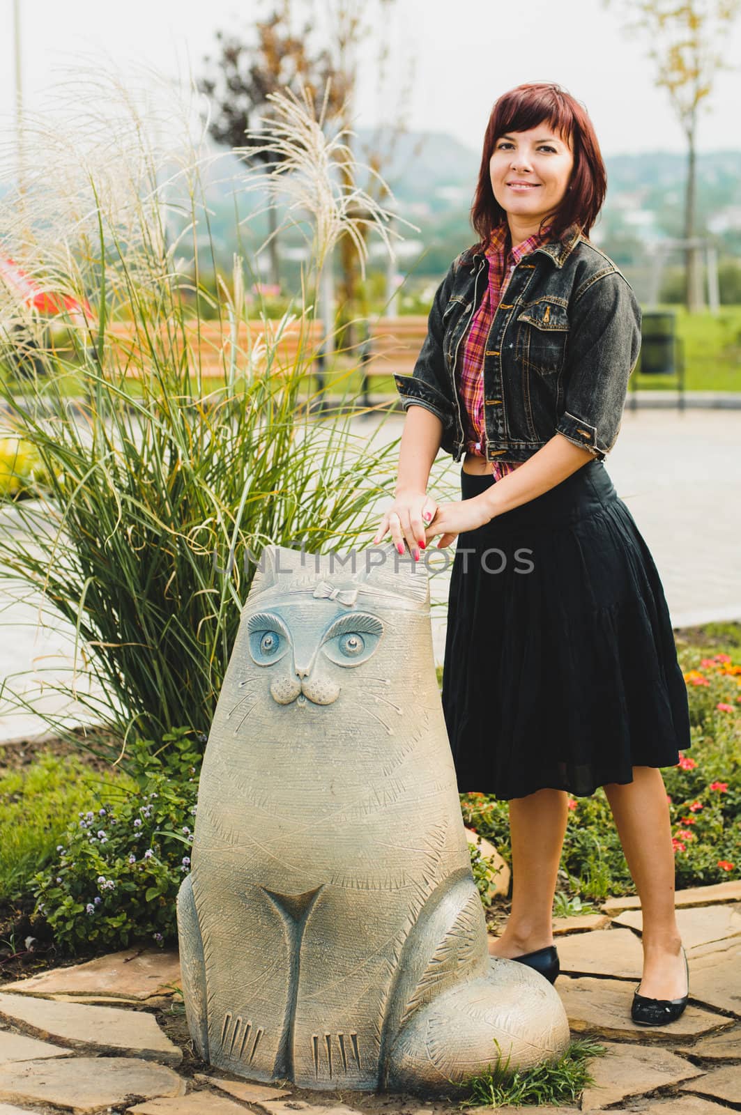 Young woman standing near funny cat statue in summer day