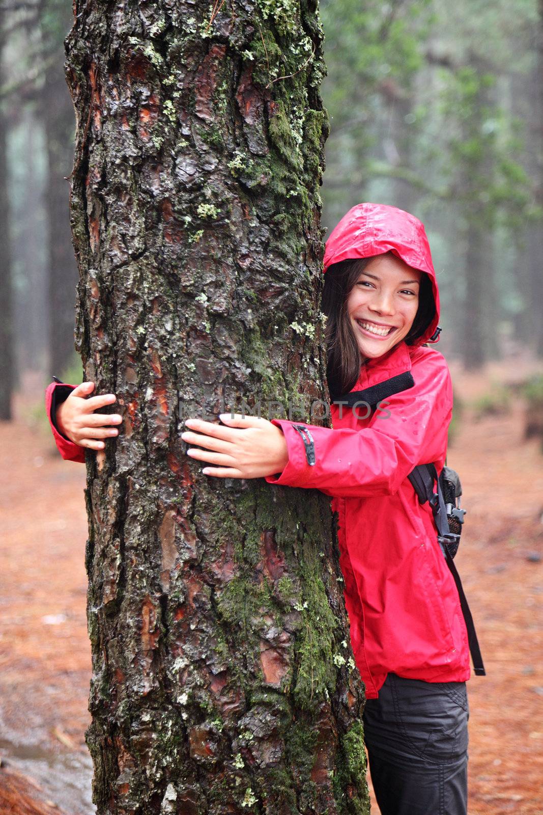 Happy beautiful young woman in an anorak standing hugging a tree in misty woodland as she strives to protect the environment and promote sustainability