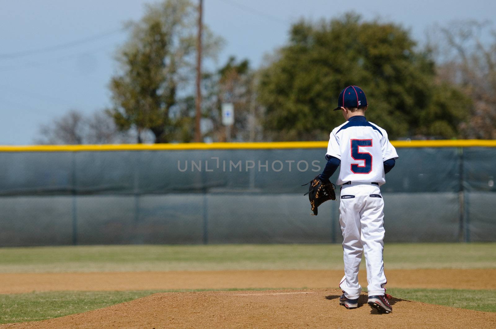 Little league baseball player taking the mound to pitch.