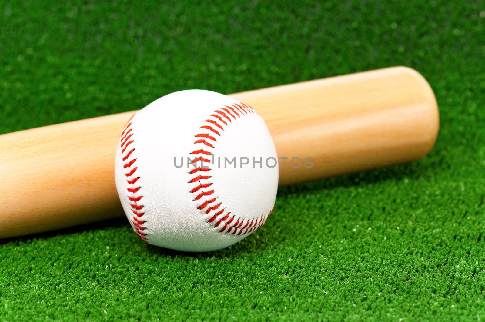 Close-up of wooden bat and baseball ball on artificial green grass