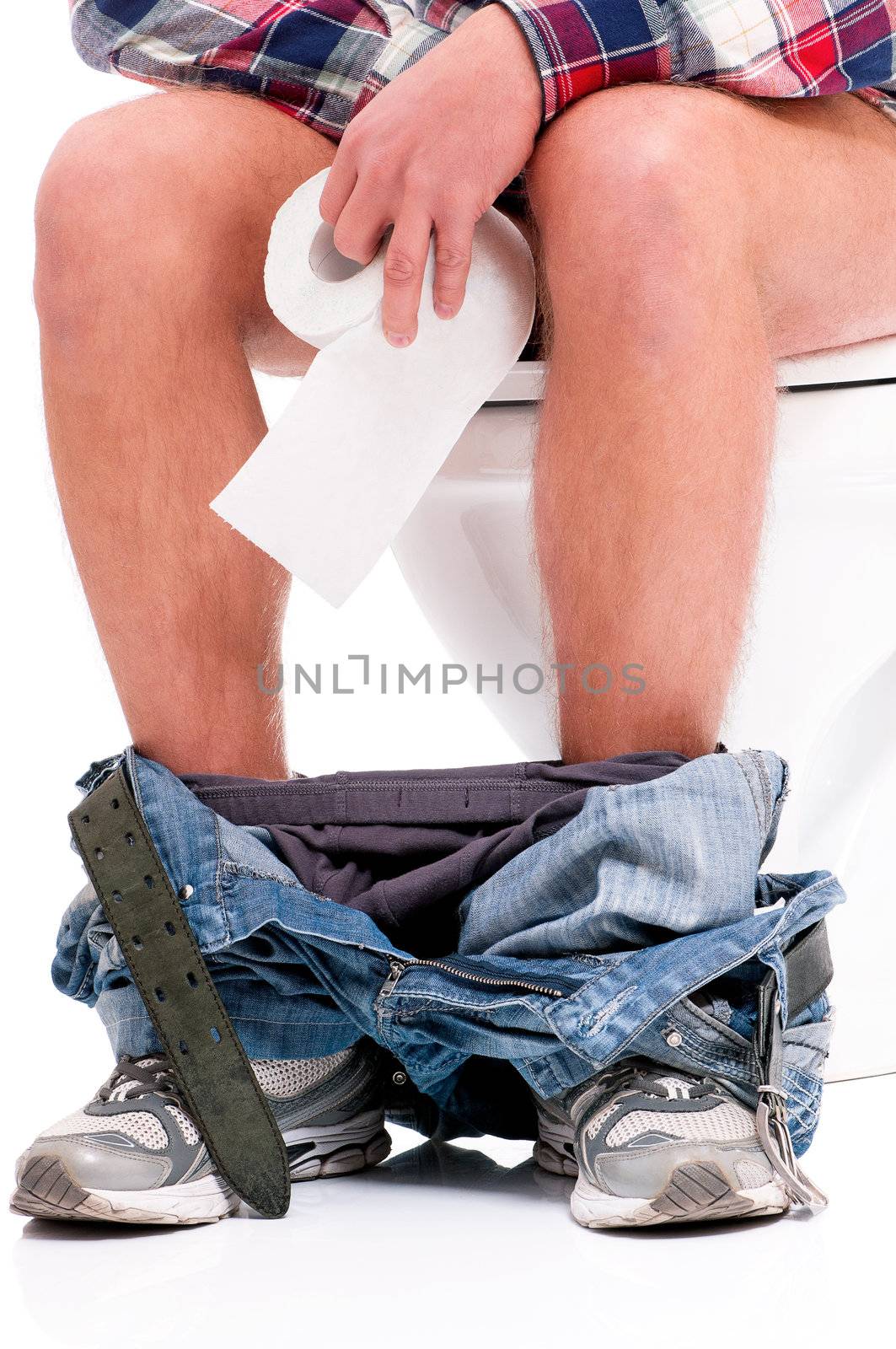 Man is sitting on the toilet bowl, holding paper in hands, on white background