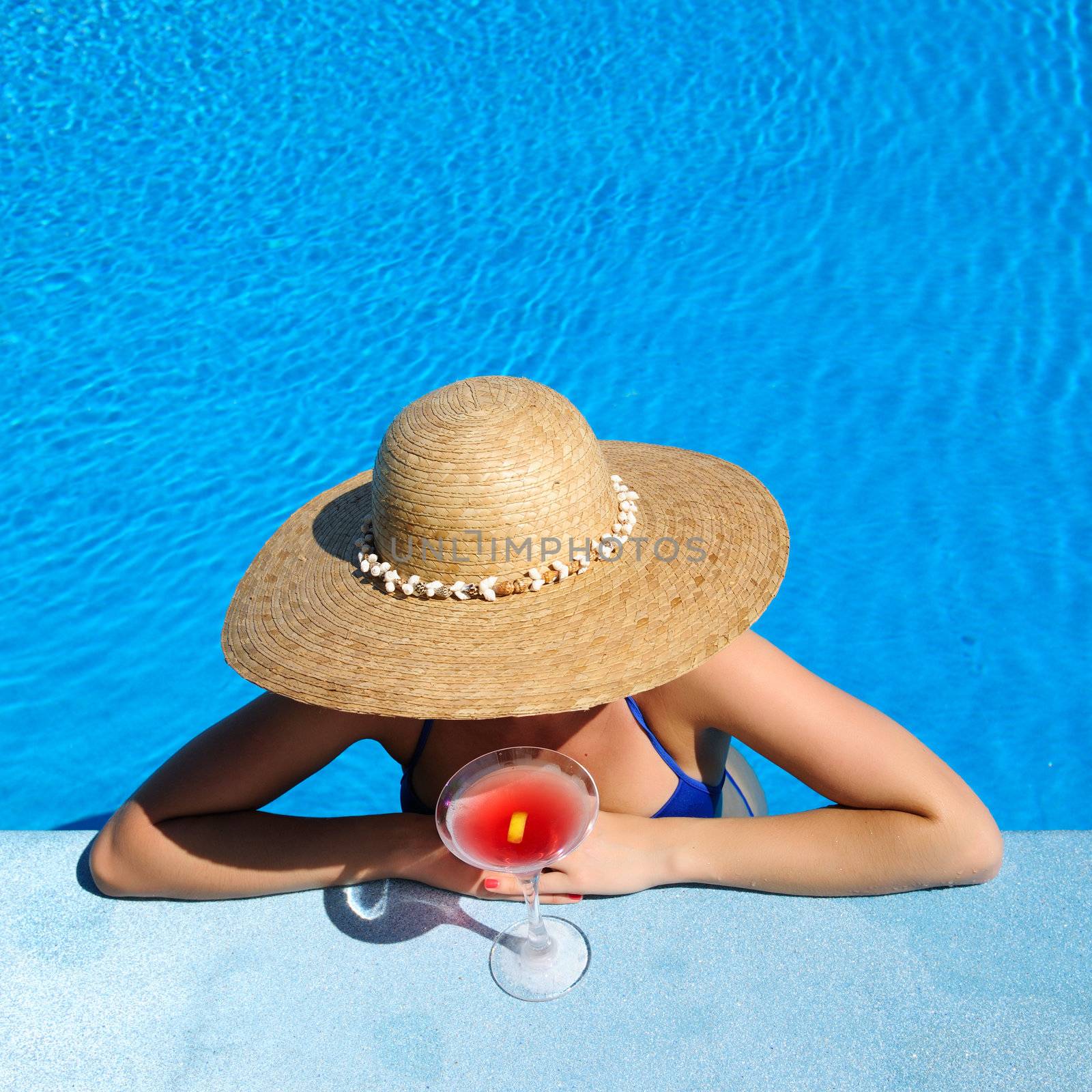 Woman in hat relaxing at the pool with cosmopolitan cocktail