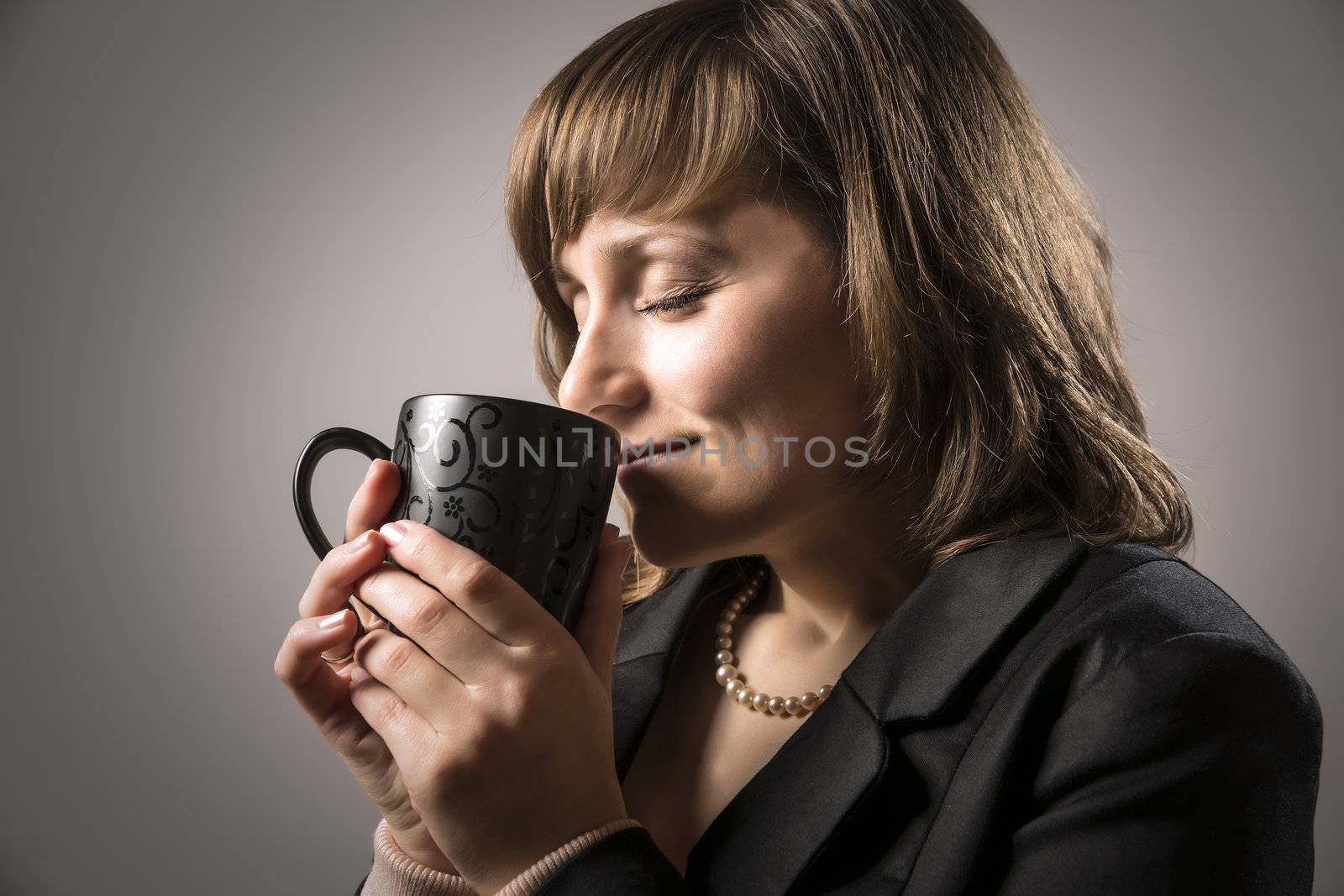 Business woman in black costume is enjoying her hot beverage