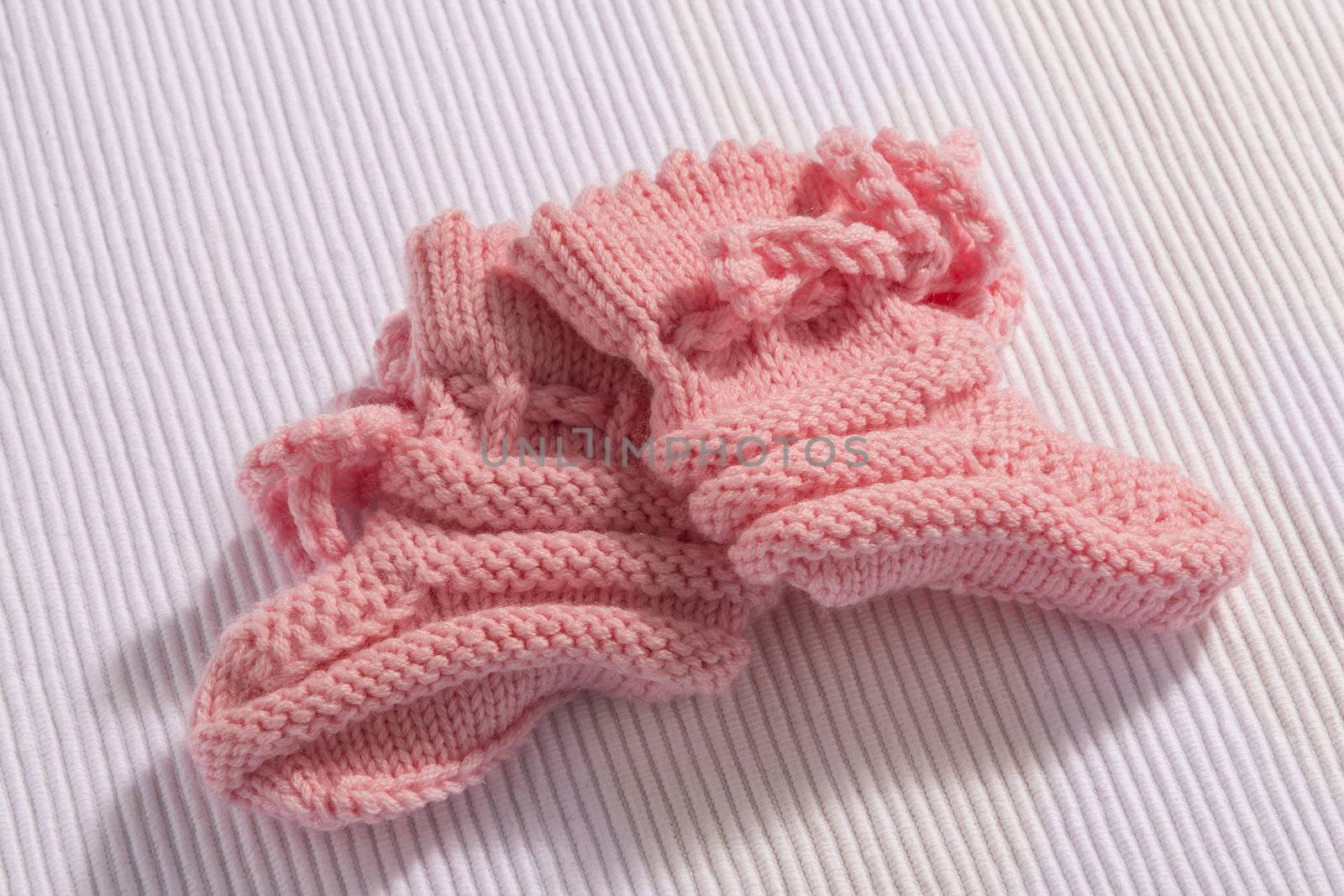 Pair of self knitted pink baby socks on white background