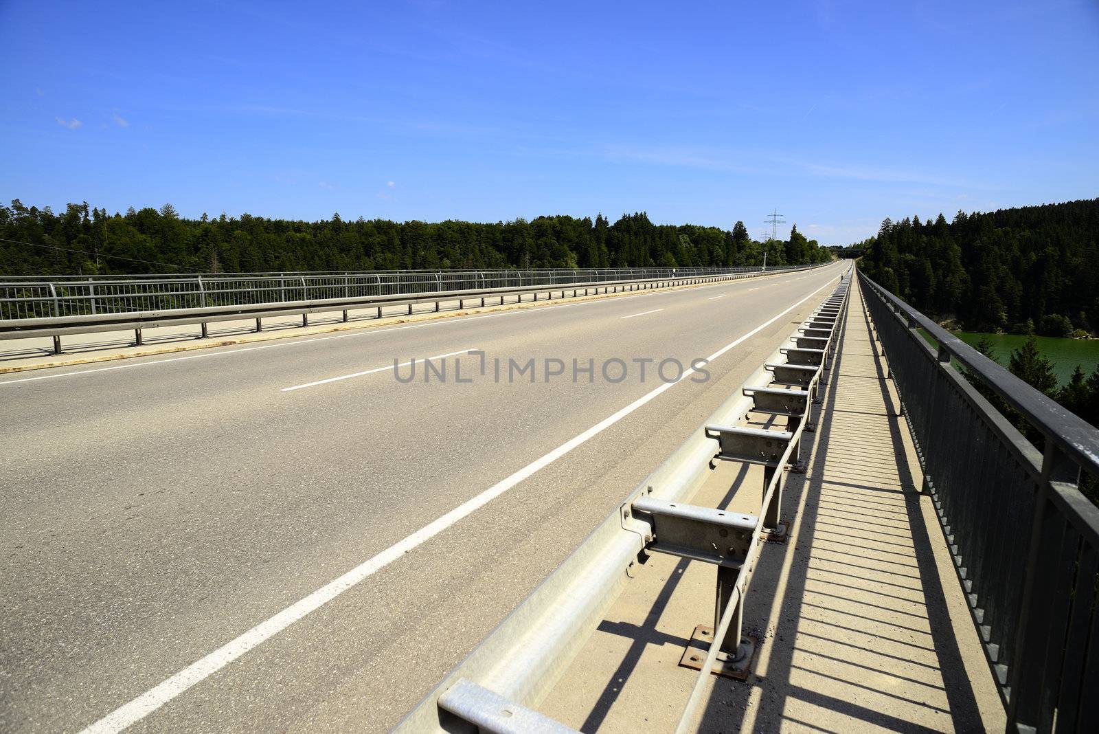Concrete road bridge over the river called "Lech". Placed in Germany, Bavaria, Allgäu. There are also coniferous trees and blue sky, sunny weather.