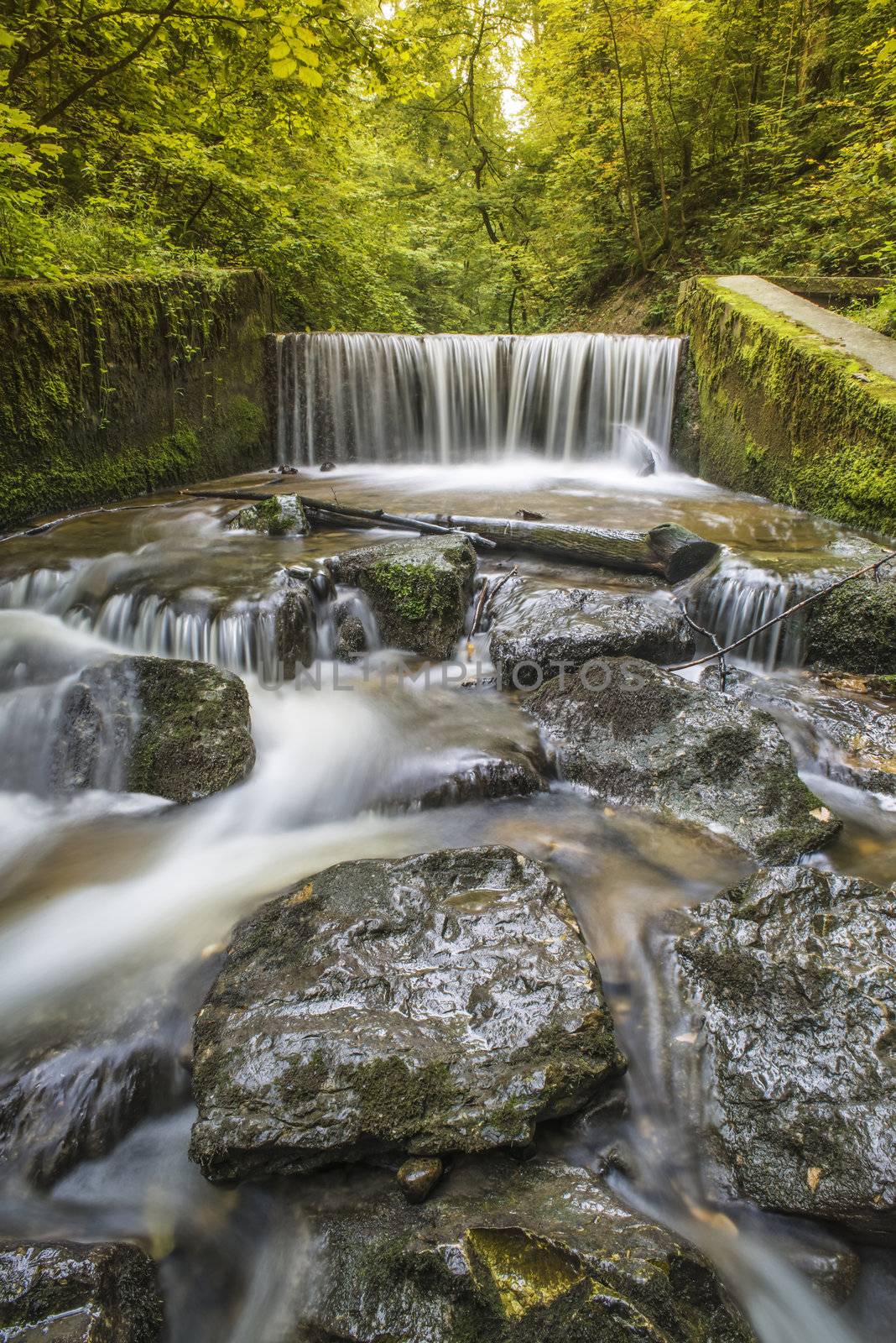 Picture with with white-angle lens of a waterfall in a forest in summer with a long exposure time.
