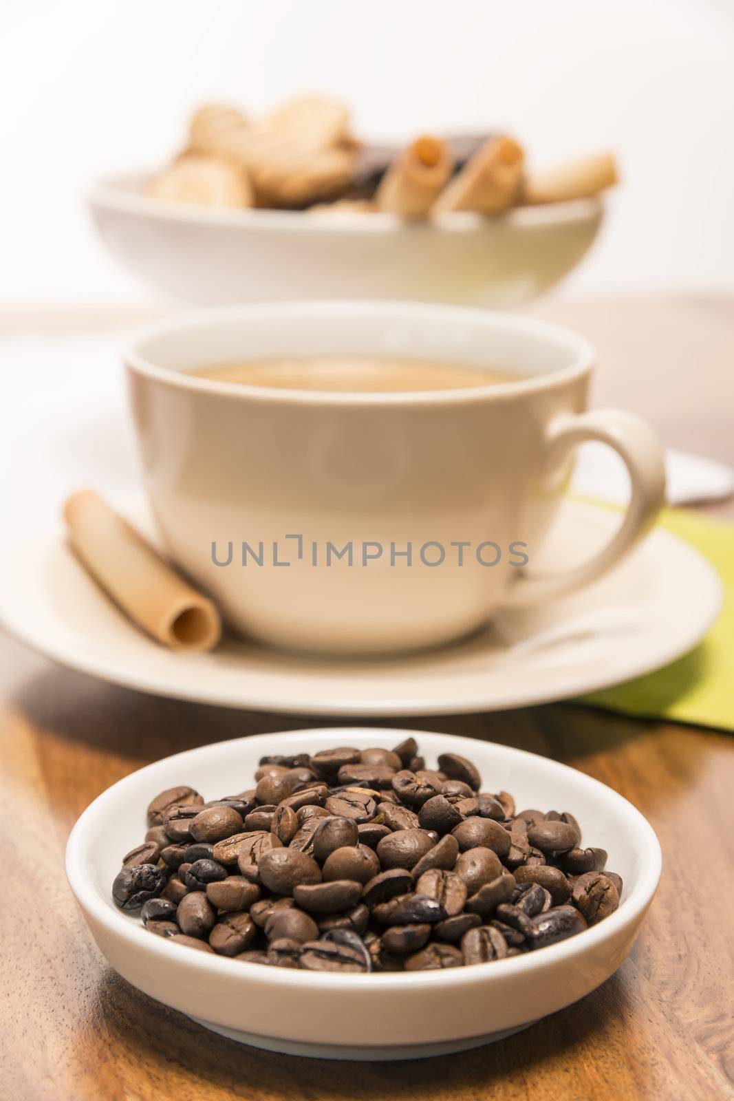 Coffee beans in a small bowl with cup of coffee and a cup of cookies