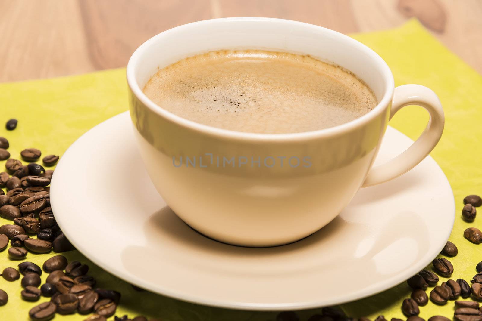 Cup of coffee with a green serviette and coffee beans on a wooden table