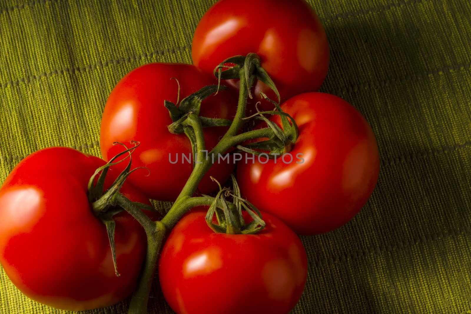 Five red tomatoes on a green tablecloth