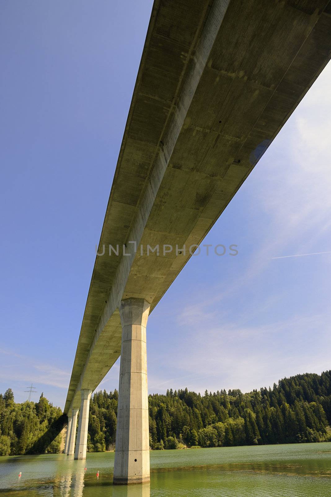 Concrete-Bridge over the river called "Lech". Bottom-up view. Placed in Germany, Bavaria, Allgäu. There are also coniferous trees and blue sky, sunny weather.