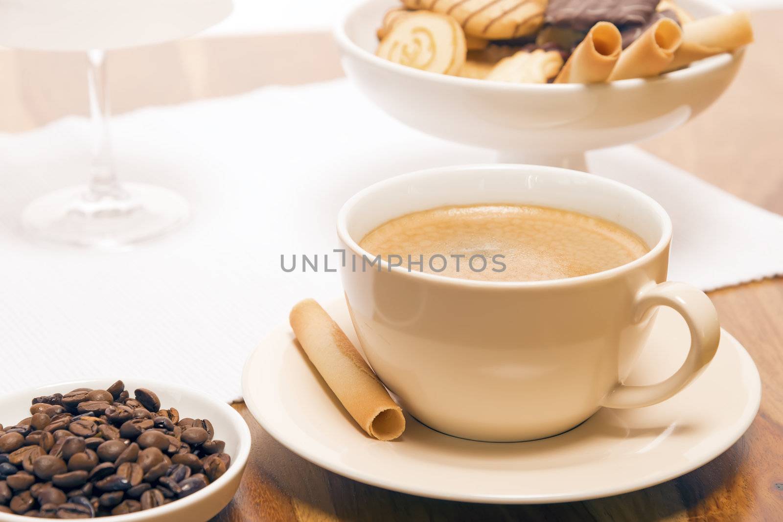 Wooden table with cup of coffee, small bowl with coffee beans and a cup of cookies