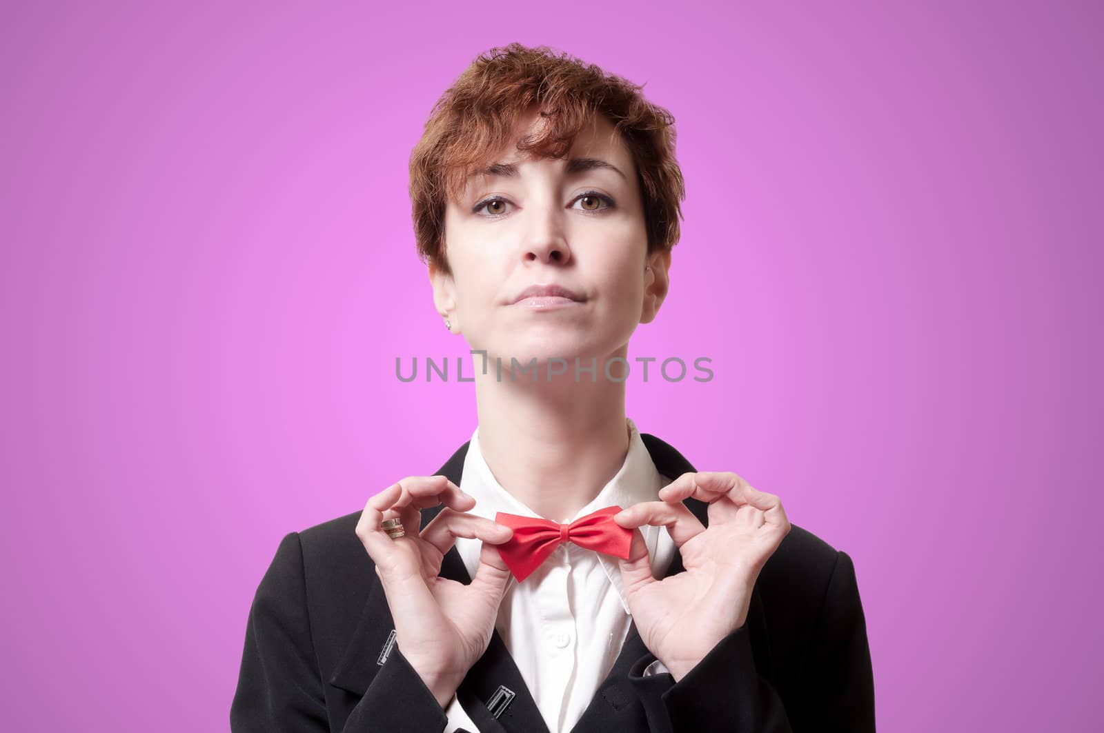 elegant businesswoman adjusting bow tie on pink background