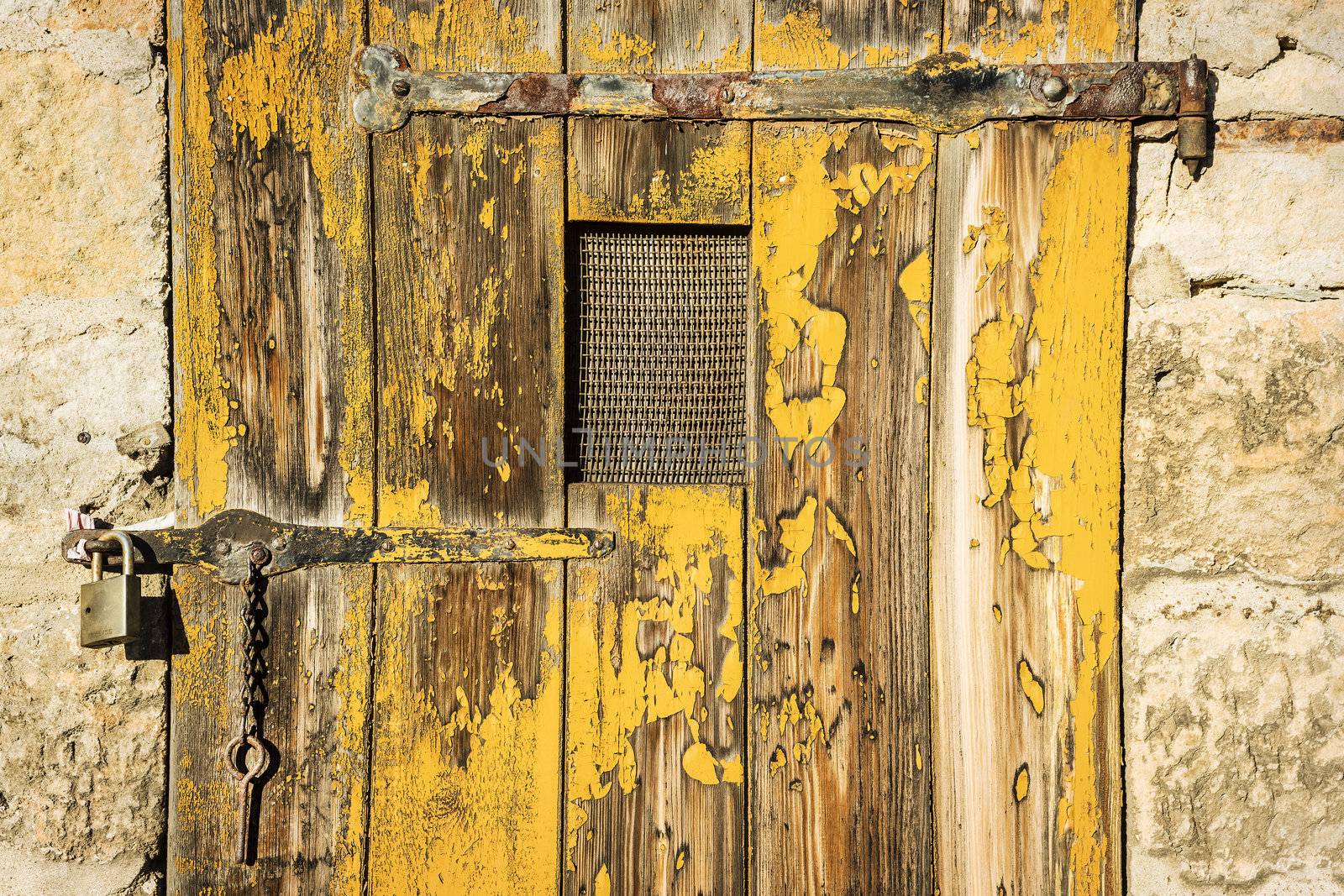 Old, weathered wooden door with yellow paint and metal fittings and lock