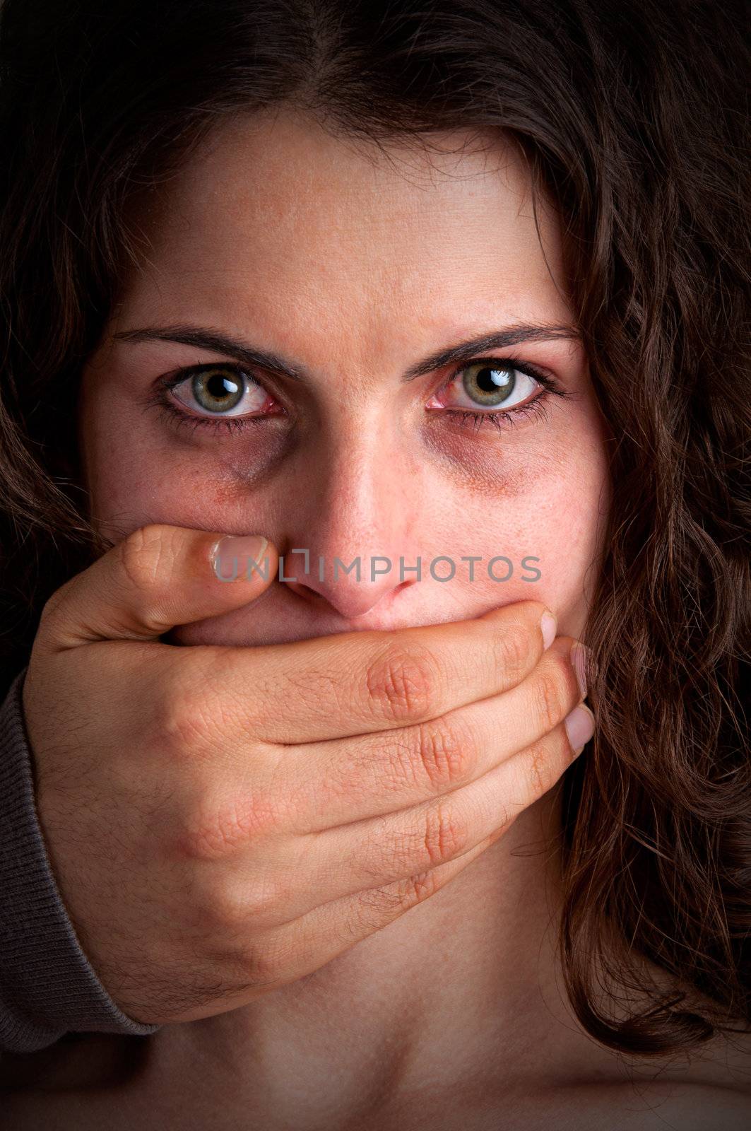 Closeup of a mans hand covering a womans mouth. Concept of domestic violence or kidnapping. Dark mood.