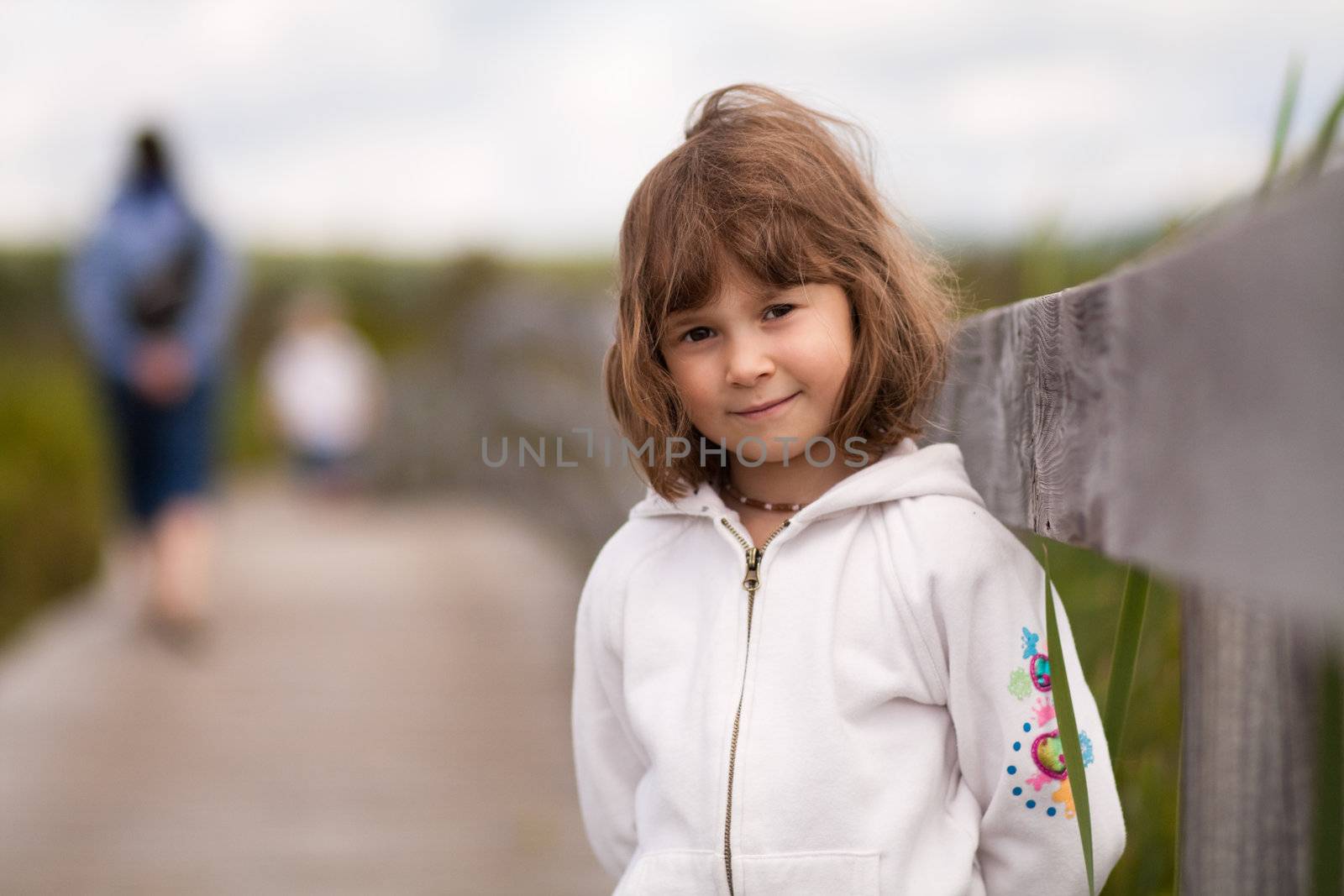 Little girl standing on a boardwalk with her mother and brother blurred in the background