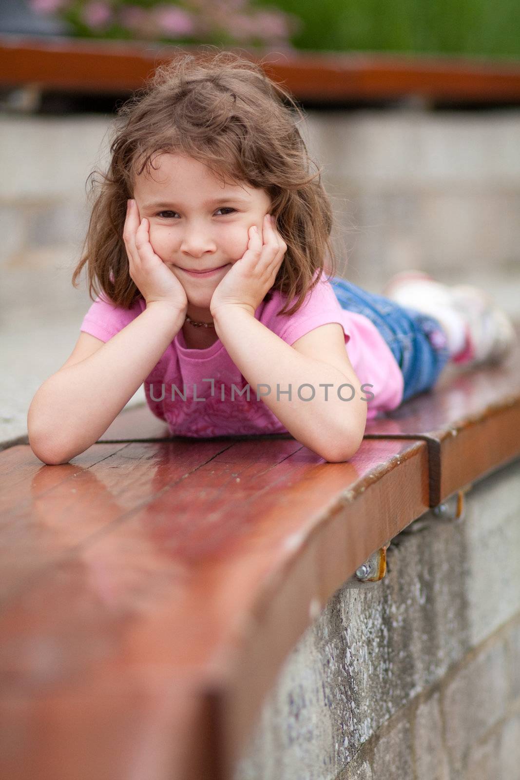 Cute little girl laying on her stomach on a park bench