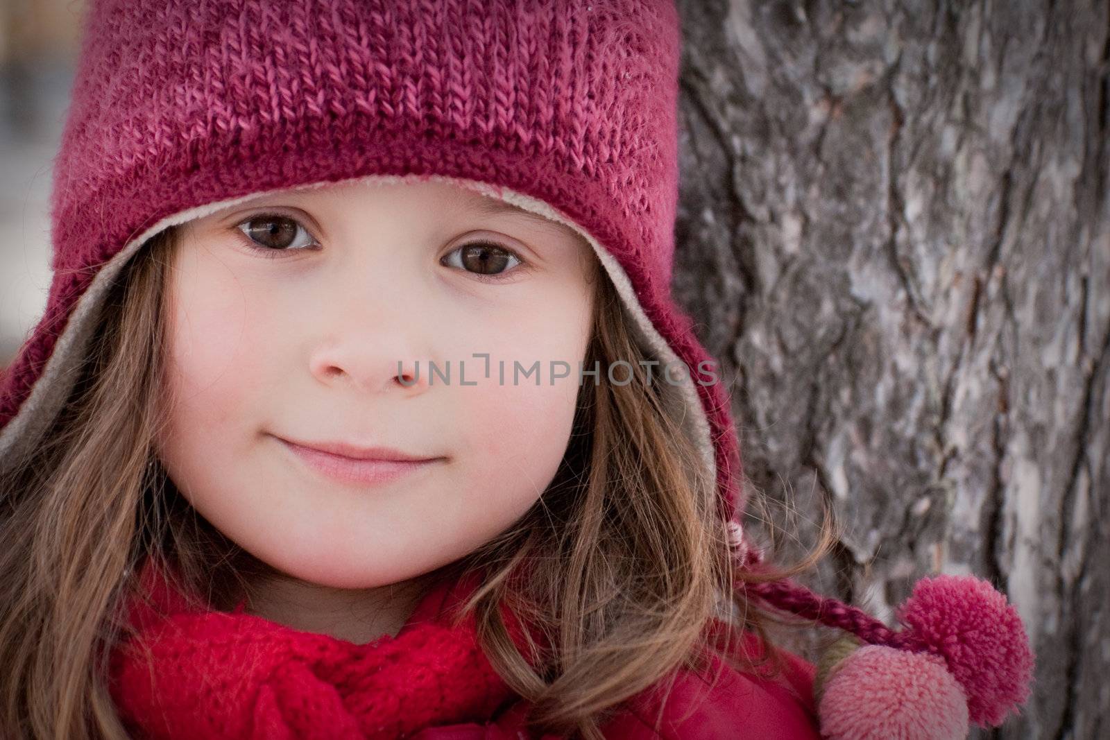 Cute little girl leaning on a tree in winter