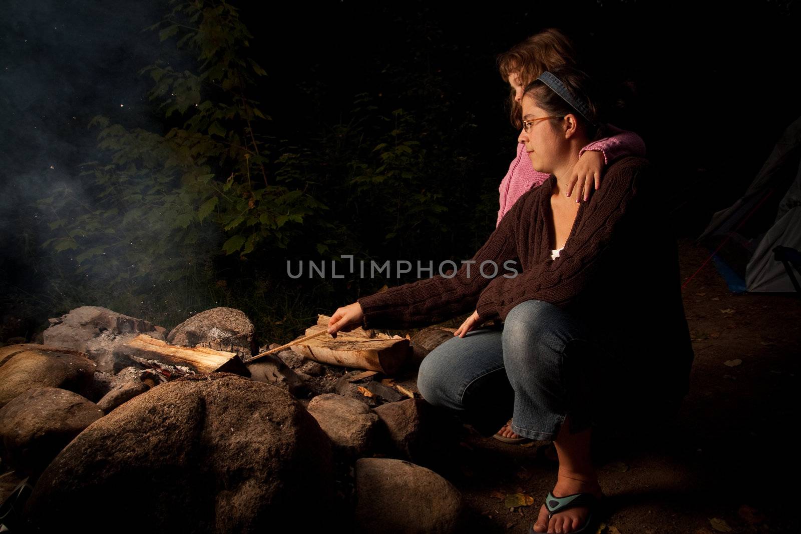 Mother and daughter tending to a campfire at night