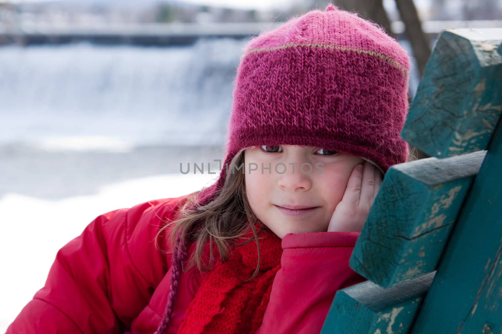 Cute little girl sitting on a bench in winter