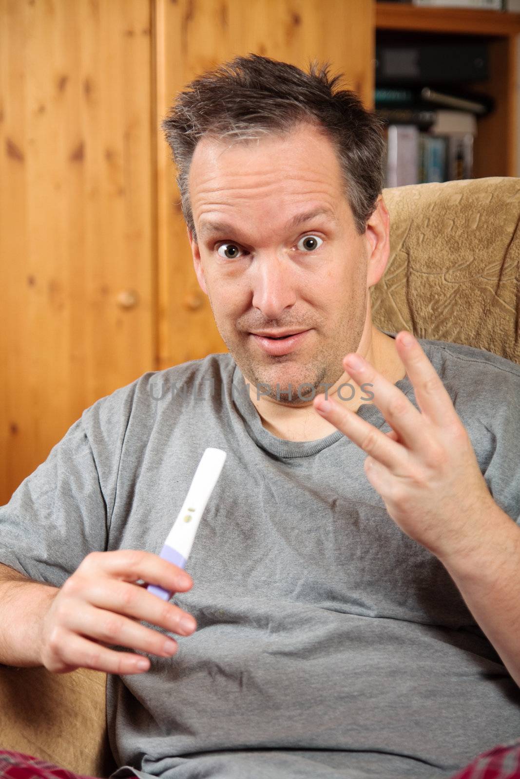 Surprised man holding a positive pregnancy test and showing 3 fingers