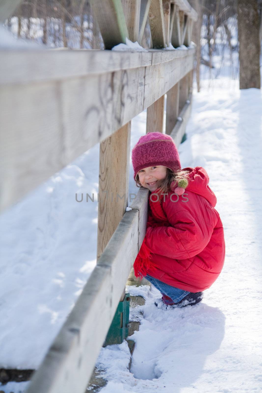 Cute little girl crouching by a fence on a wooden bridge
