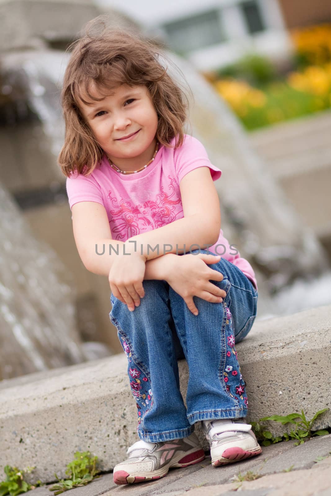 Cute little girl sitting in front of an urban waterfall