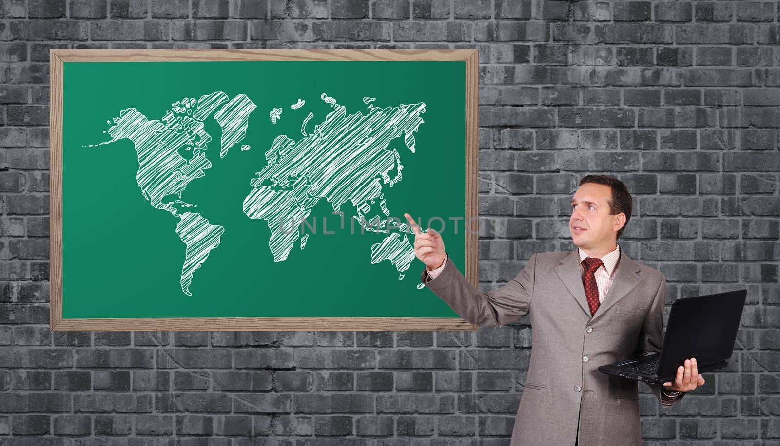businessman with a laptop in hand points to word map on blackboard