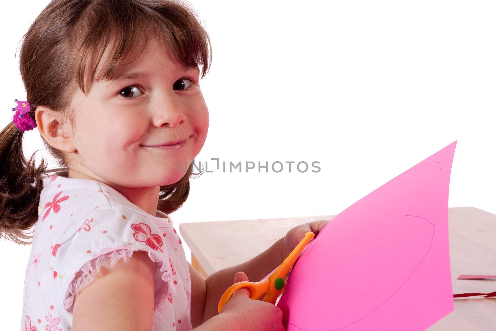 Cute little girl cutting out hearts in pink paper