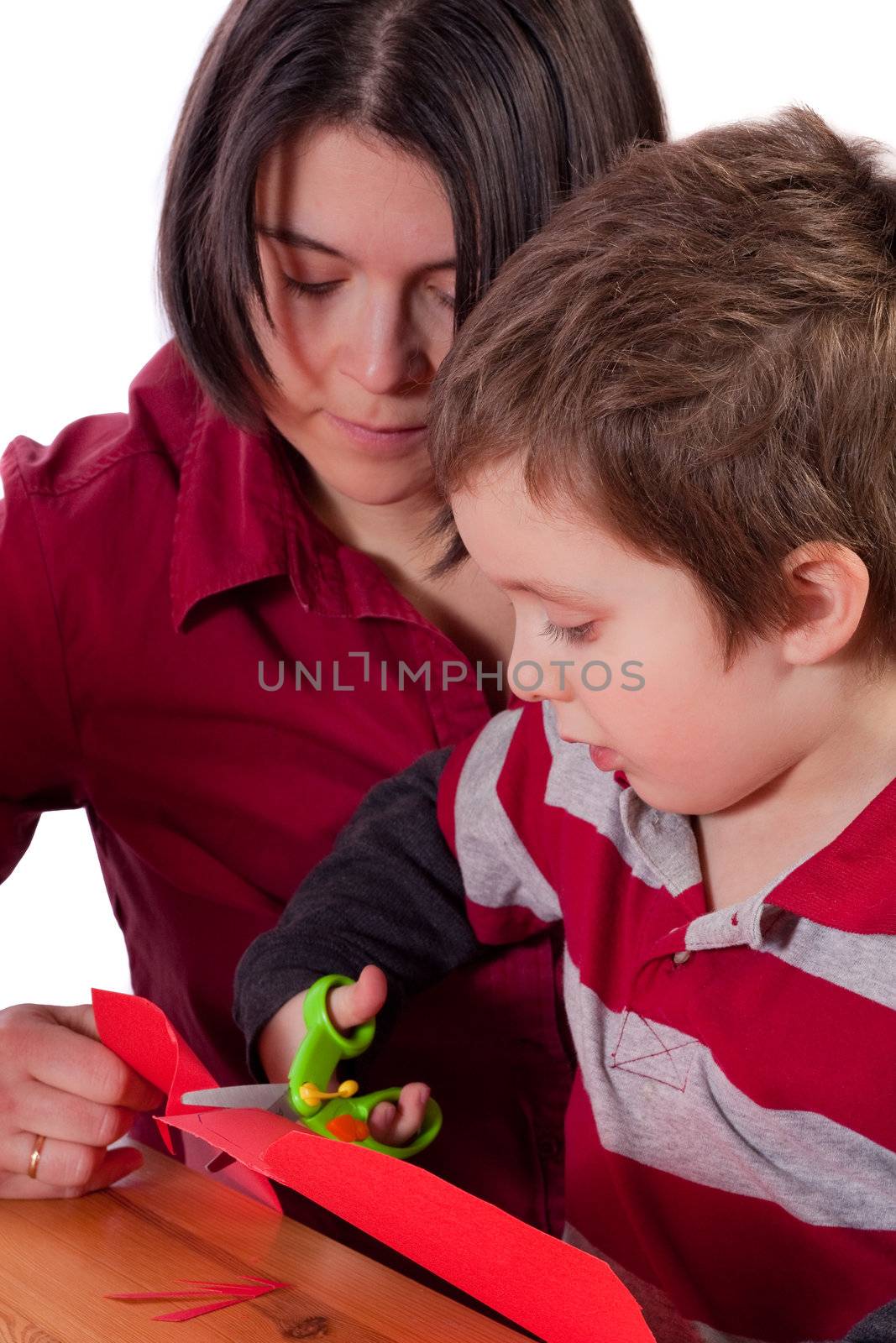 Mother helping her son to cut out a red heart in cardboard