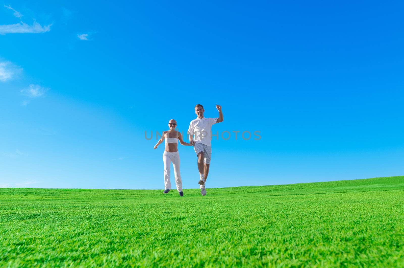 Happy couple jumping together holding hands on a green field