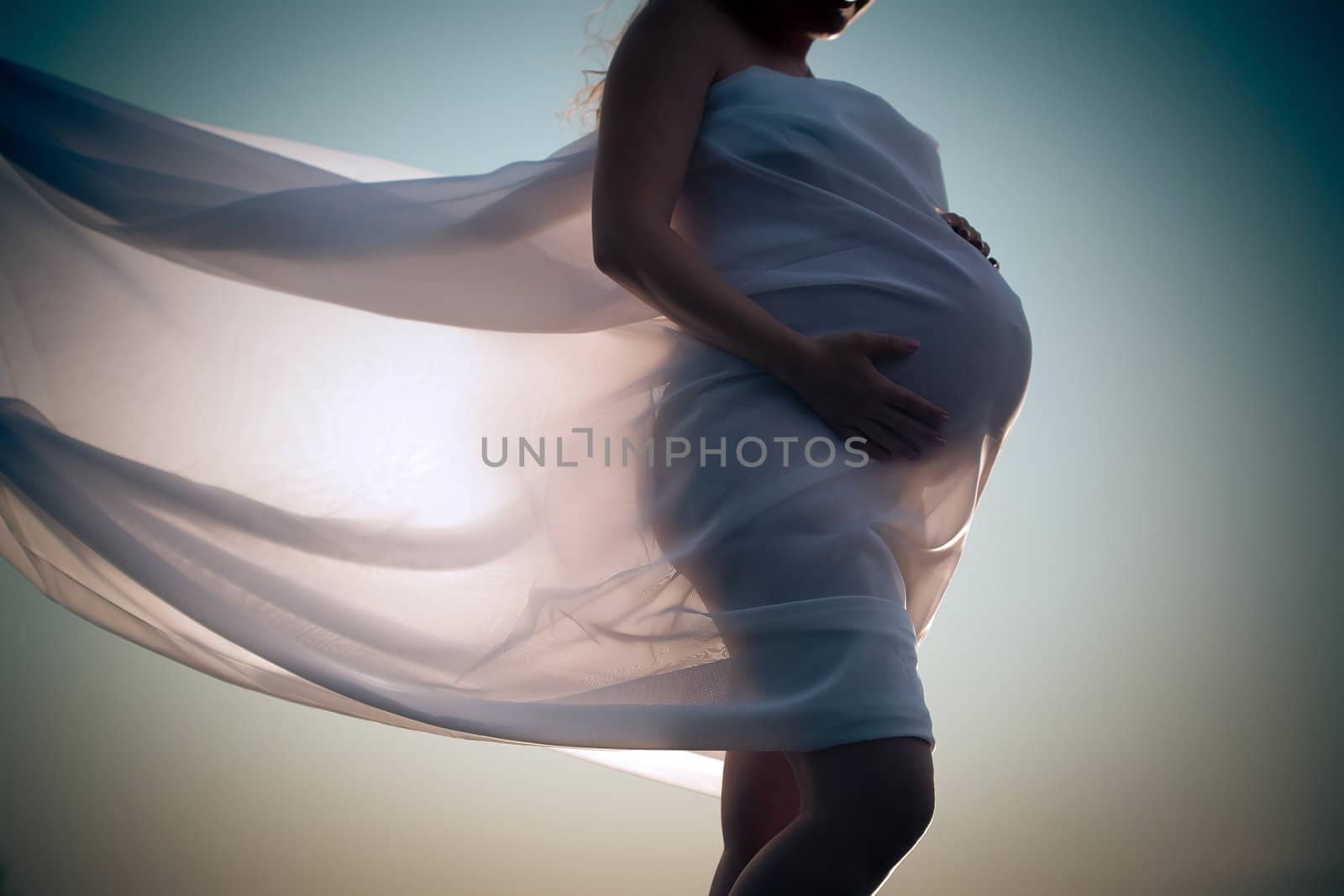 Pregnant woman wrapped in veil holding her belly with arms
