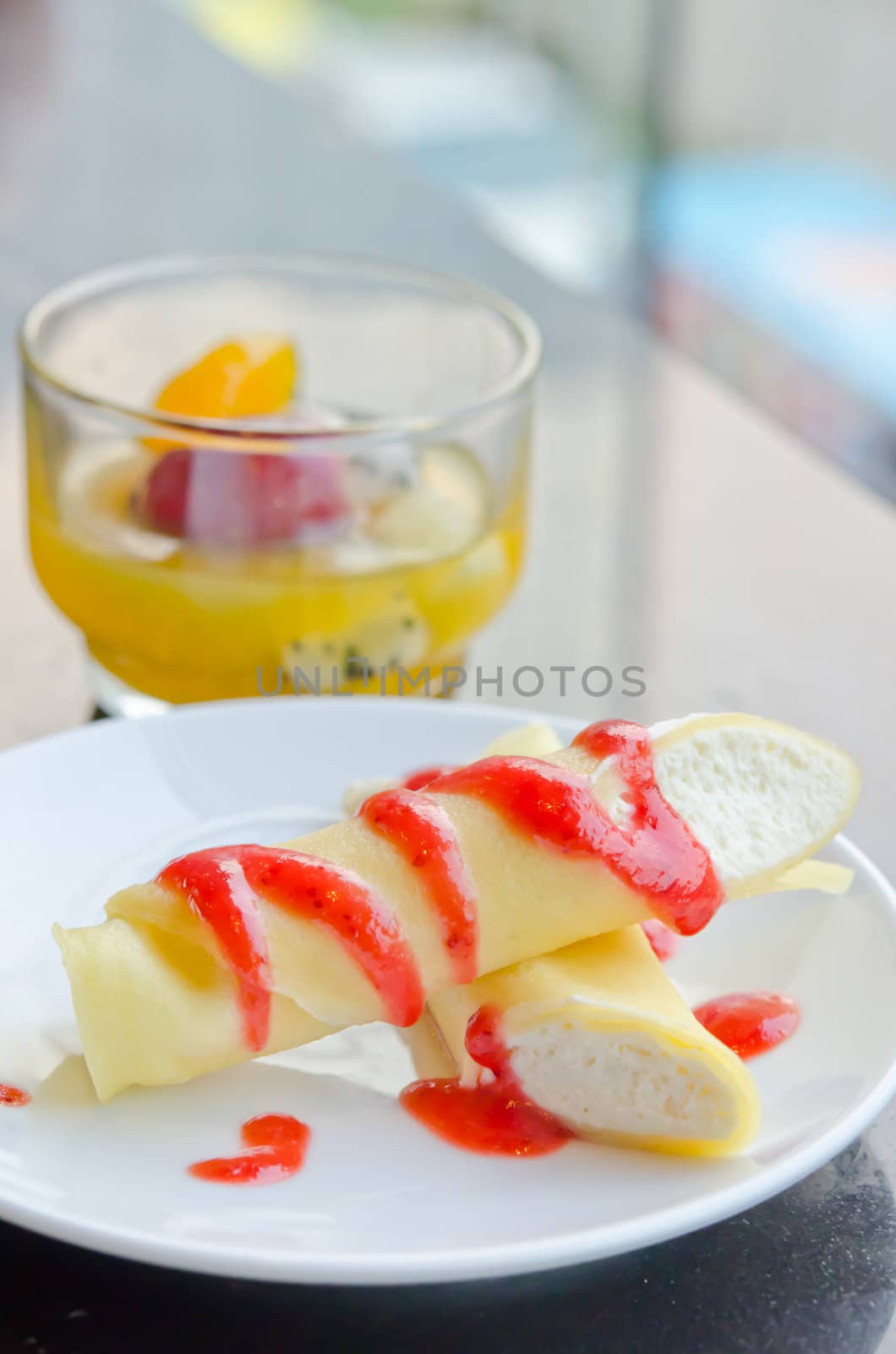 the roll pancakes with the strawberries syrup and cream on dish  and mix fruits in glass ,  dessert on table