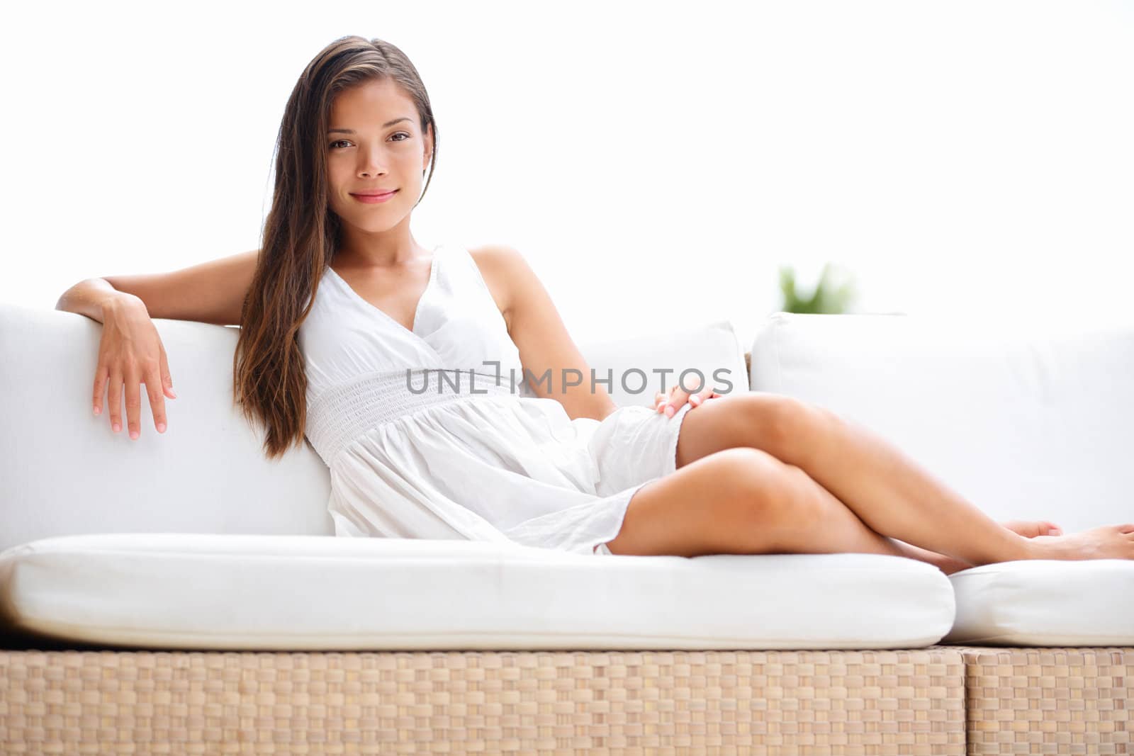 Woman luxury living lifestyle lying on sofa outside smiling confident at camera. Beautiful multicultural young elegant woman in white dress outdoors.