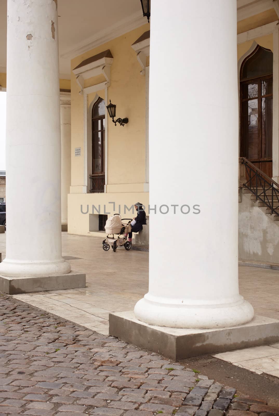 Woman with baby carriage next to a colonnade in Odessa