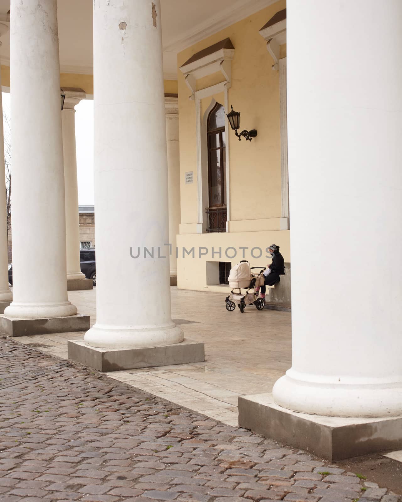 Woman with baby carriage next to a colonnade in Odessa