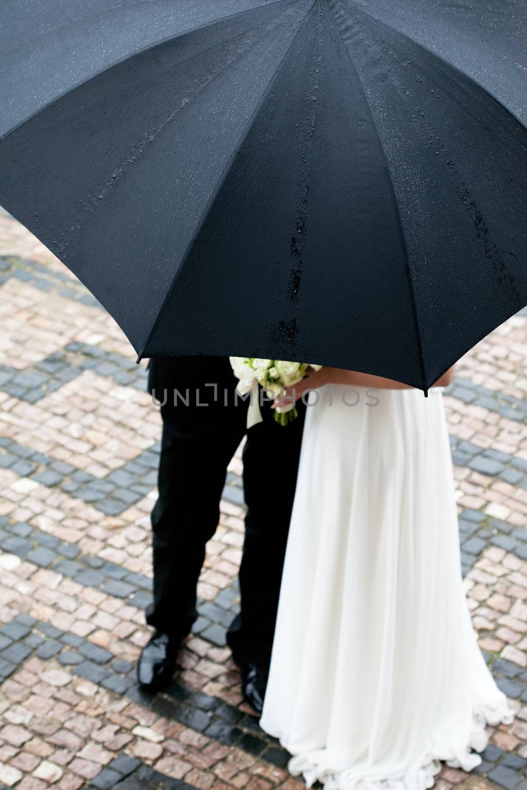 the bride and groom with a bouquet of flowers under the umbrella by jannyjus