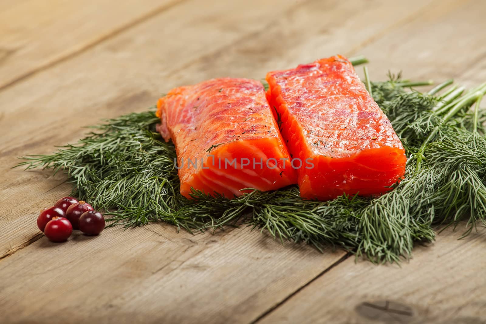 Two pieces of salty salmon with greenery and cranberry on the old wooden table
