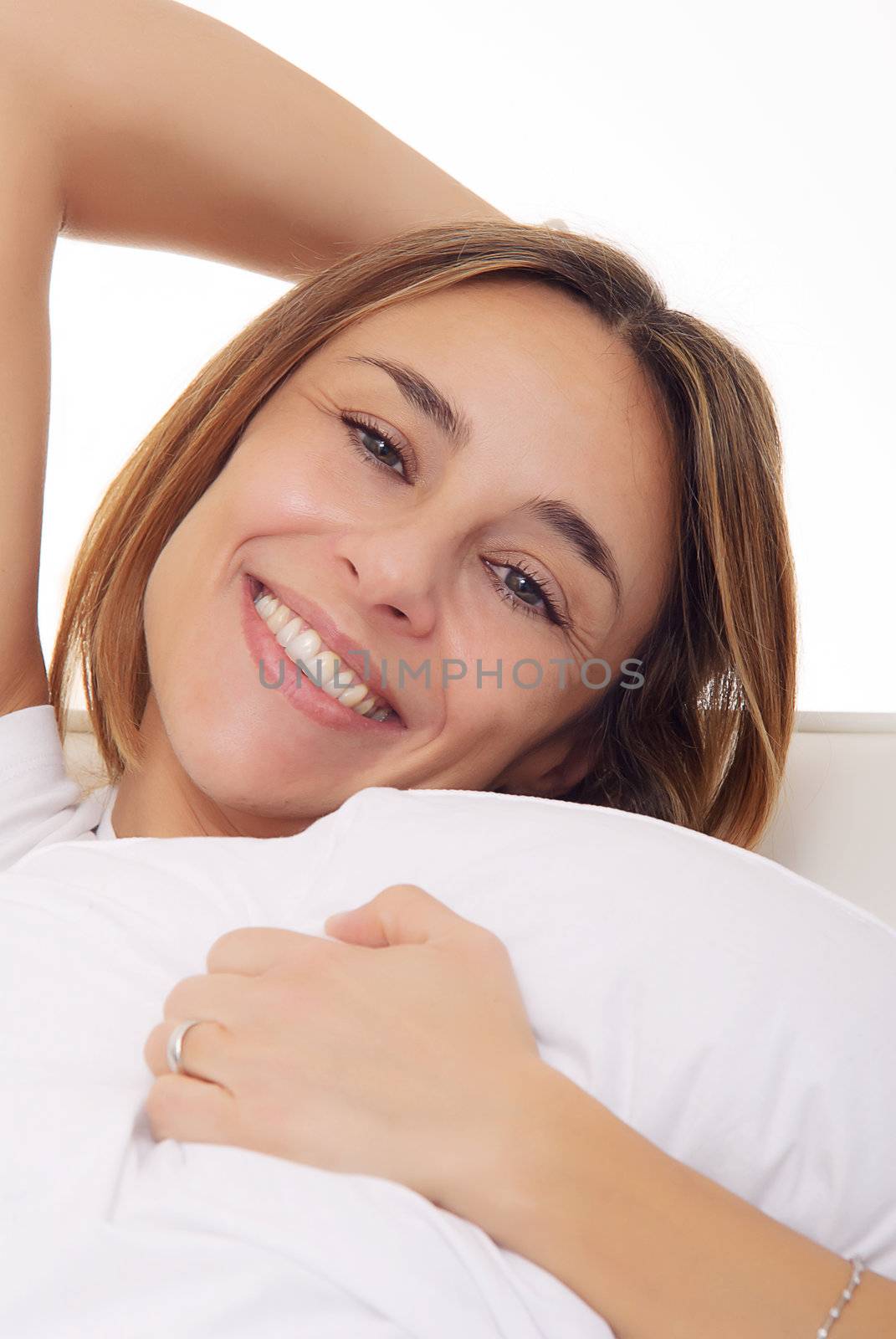mature lady smiling and cuddling a pillow on couch by matteobragaglio