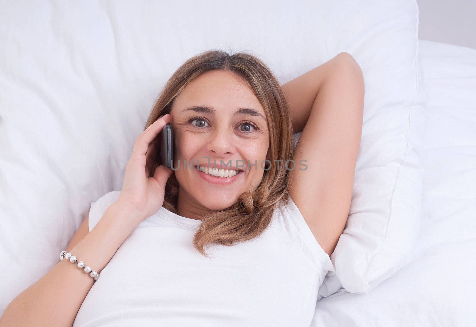 Beautiful happy young woman smiling and using her cell phone at home on her sofa