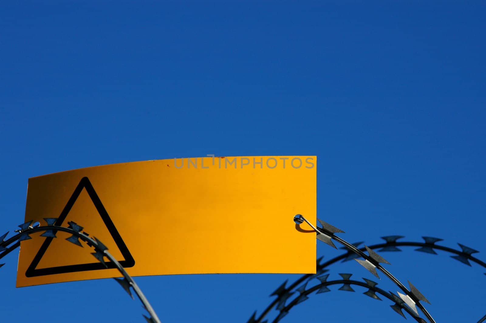 A Blank Yellow Warning Sign on Some Razor Wire