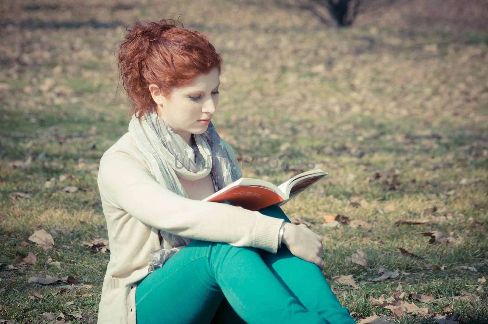 red long hair girl at the park reading in spring 