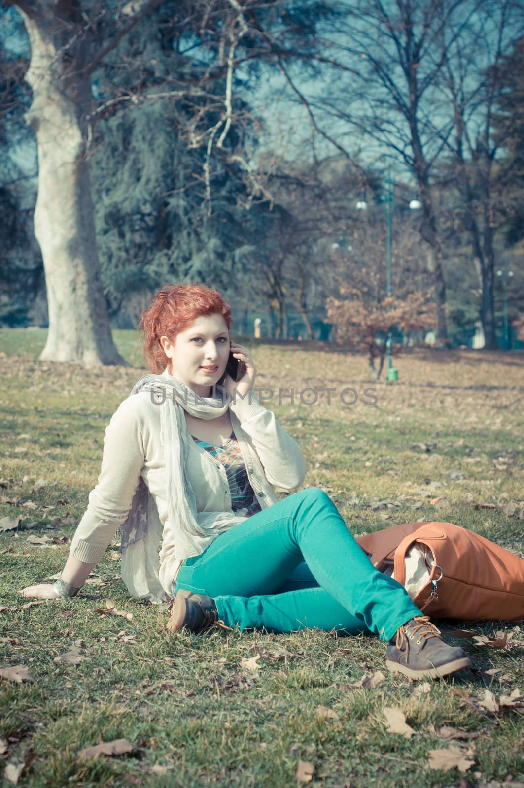 red long hair girl at the park on the phone in spring 