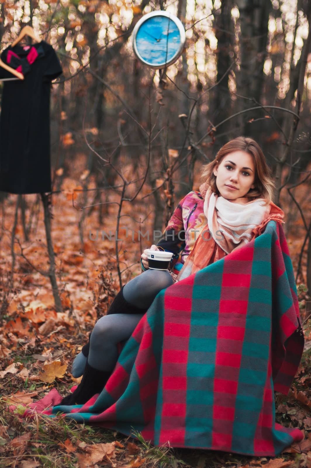 Beautiful girl sitting on armchair in autumn forest with cup in her hands