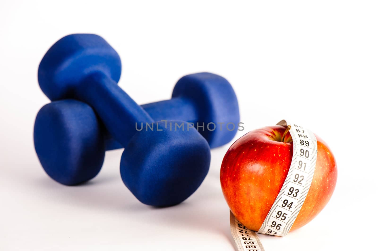 Blue dumbbells and red apple with measure tape isolated on a white background